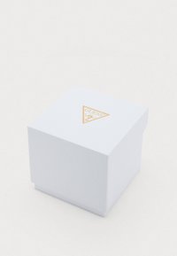 Caixa de presente branca em forma de quadrado, feita de material texturizado, com um logótipo triangular dourado e o texto "GUESS" na tampa.