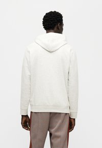 Ανοιχτό γκρι φούτερ με κουκούλα και κορδόνια, καθώς και με ριμπ μανσέτες. Συνδυάζεται με παντελόνι με καρό σχέδιο. Απλός, casual σχεδιασμός.