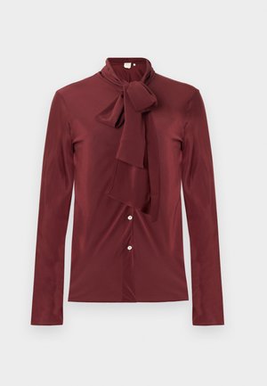 Dieprode blouse met lange mouwen en een strikcol, gemaakt van een soepele stof. Heeft een knoopsluiting aan de voorkant en een getailleerde pasvorm.