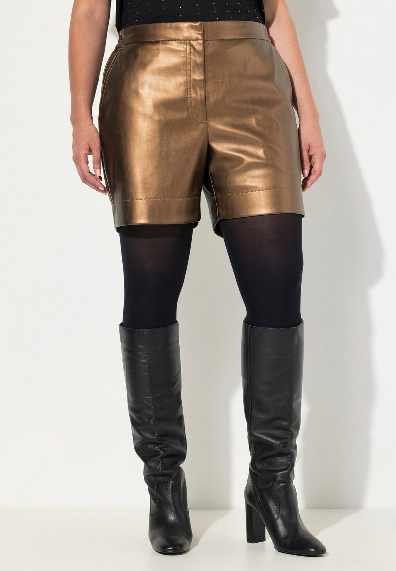 Bronzen nepleer short met een gladde textuur, met een hoge taille en rechte snit. Gepaard met zwarte ondoorzichtige panty’s en zwarte laarzen tot de knie.
