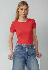 Czerwona, prążkowana koszulka z krótkim rękawem w połączeniu z dżinsami z wysokim stanem w kolorze niebieskim. Top ma okrągły dekolt i dopasowany krój, podkreślający fakturę.