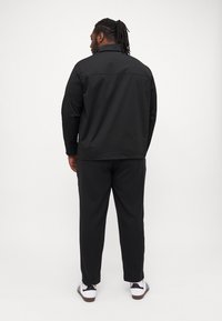 Svart lett jakke med krage, kombinert med svarte bukser. Antrekket har en avslappet passform og er supplert med hvite joggesko.