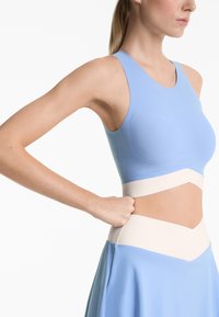 Blue sports top with a smooth texture, featuring a cutout design and contrasting beige band around the waist. Minimalist sleeveless style.