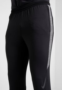 Zwarte sportbroek met een aansluitend ontwerp, voorzien van een gestructureerde grijze streep langs de zijkant en een elastische tailleband voor comfort.