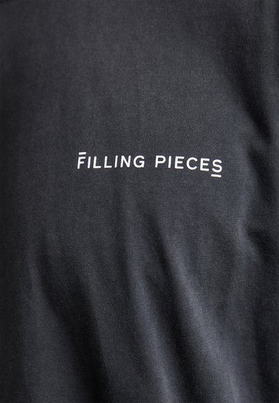 Tissu en coton noir avec une texture lisse présentant le texte blanc "FILLING PIECES" dans une police moderne, centré.