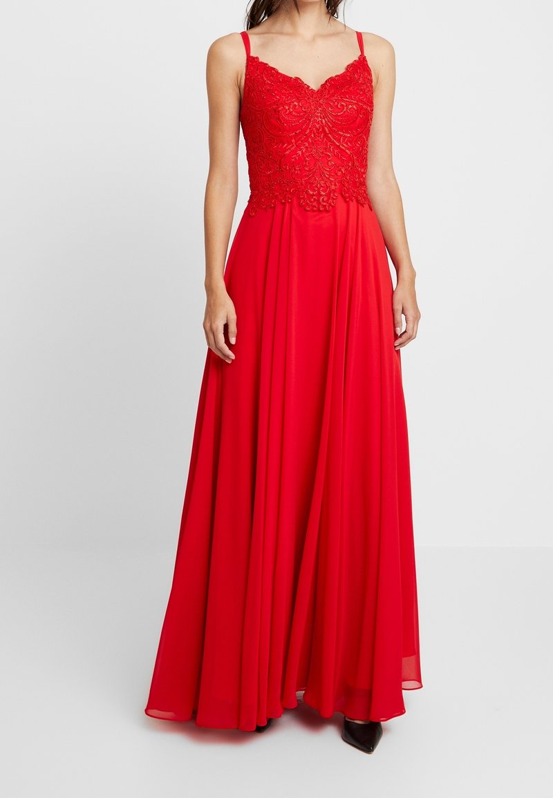 Robe de soirée rouge avec un corsage ajusté et orné, et une jupe en chiffon fluide. Présente des bretelles fines et un décolleté en cœur.