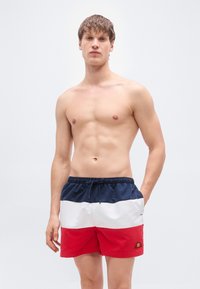 Ανδρικά μαγιό βερμούδα σε ναυτικό μπλε, λευκό και κόκκινο με ελαστική μέση και ρυθμιζόμενο κορδόνι. Διαθέτουν λεπτομέρεια με λογότυπο στο αριστερό πόδι.