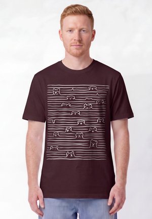 Man with red hair wearing a dark brown T-shirt featuring white line drawings of different dog faces between horizontal lines.