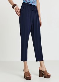 Pantalon bleu marine fuselé avec taille élastique, cordon de serrage et texture lisse, associé à des sandales à plateforme marron.
