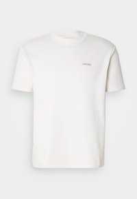 Jednoduché bílé tričko s krátkým rukávem, kulatým výstřihem a malou nášivkou s logem "Calvin Klein" na levé části hrudníku.