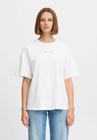 Bílá bavlněná tričko, oversize střih, krátké rukávy. Na přední straně je vytištěno "1983 - LONDÝN" v malém, kontrastním písmu.