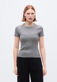 Γκρι κοντομάνικη ριμπ μπλούζα με στρογγυλή λαιμόκοψη διακοσμημένη με πολύτιμους λίθους, με εφαρμοστή σχεδίαση και απαλή υφή, συνδυασμένη με μαύρο παντελόνι.