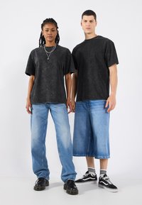 Tricouri negre, supradimensionate, cu mânecă scurtă, dintr-un material texturat; asortate cu blugi albaștri deschiși și pantaloni scurți din denim. Încălțămintea include cizme negre și adidași.