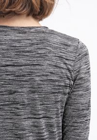 Personne aux cheveux courts châtain clair portant un t-shirt à manches longues gris et noir chiné, ajusté, vue de dos.