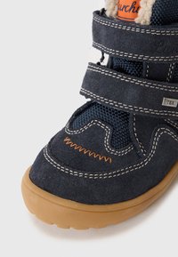 Dunkelblaue Kinderschuhe aus Wildleder, mit strukturierten Mesh-Akzenten, zwei Klettverschlüssen, orangefarbener Naht und einer gummierten, hellbraunen Sohle.