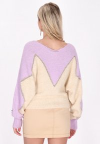 Weich gestrickter Pullover mit einem Farbmix aus Flieder und Creme, der ein Sternmotiv und Fransenverzierungen am Saum aufweist.