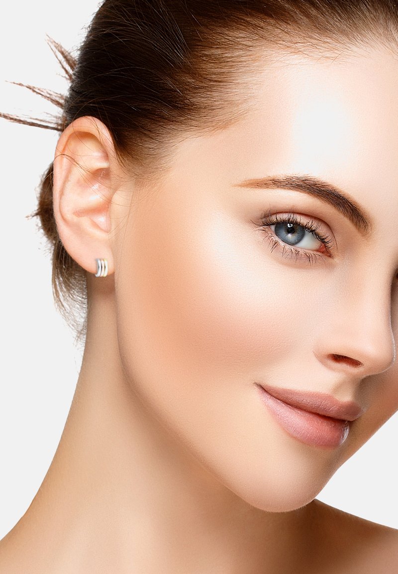 Elegant silver studs med tre horisontella band, mot en mjukt fokuserad bakgrund. Slät, lysande hud och naturlig makeup.