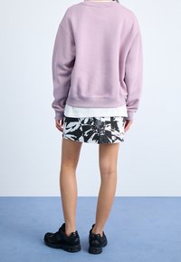 Sudadera rosa clara de gran tamaño con puños acanalados, superpuesta sobre una camisa blanca. Falda con estampado floral en blanco y negro, combinada con zapatillas negras.