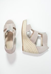 I sandali con zeppa in suede beige presentano un tacco avvolto in juta, punta aperta e una chiusura con zip sul lato con dettagli intagliati per la traspirabilità.