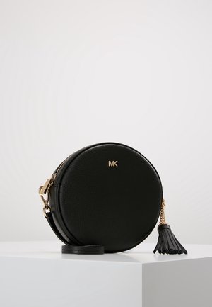Sac bandoulière rond en cuir noir avec logo MK doré, fermeture éclair dorée et pampille en cuir noir sur une surface blanche.