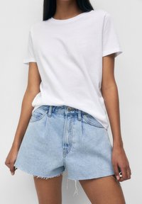 Valkoinen puuvillapaita yhdistettynä vaaleansinihin farkkushortseihin, joissa on repsottava helma, haalistunut pinta ja etunepparikiinnitys.