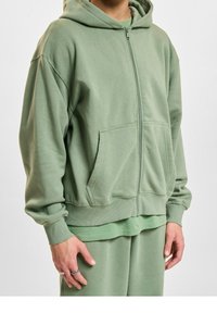 Lichtgroene rits-trui gemaakt van zachte stof, met een comfortabele pasvorm, voorzakken en geribbelde mouwen en onderkant.