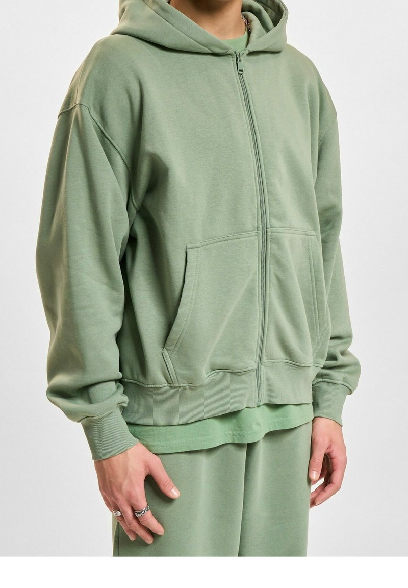 Lichtgroene rits-trui gemaakt van zachte stof, met een comfortabele pasvorm, voorzakken en geribbelde mouwen en onderkant.