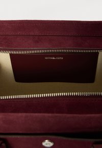 Unutrašnjost smeđe kože torbe s laganom tkaninom postavom i utorom za karticu sa upečatljivim logom "MICHAEL KORS" u srebrnoj boji.