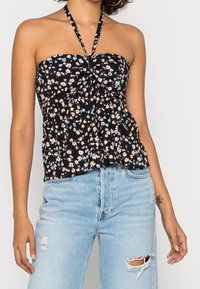 Top a halter nero con fiori rosa e blu, scollatura arricciata e orlo svasato, abbinato a jeans leggeri blu chiarissimi con effetto usurato.