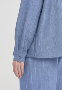 Lichtblauw, gestructureerd stoffen shirt met lange mouwen, voorzien van subtiele verticale strepen, knoopmanchetten en een ontspannen pasvorm.