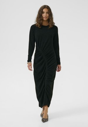 Lang schwarzes Kleid mit strukturiertem Finish, langärmlig, mit einer gedrehten Gestaltung an der Vorderseite und Midi-Länge. Ein Paar gestreifte High Heels.