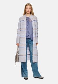 Light gray, long knit coat with blue and beige stripes; textured fabric. Paired with a ruffled blue blouse and blue flared jeans.