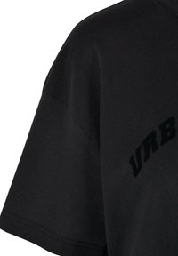 T-shirt en coton noir avec une coupe décontractée. Présente des manches courtes et un texte imprimé "URB" avec une finition brillante sur le bas du devant.