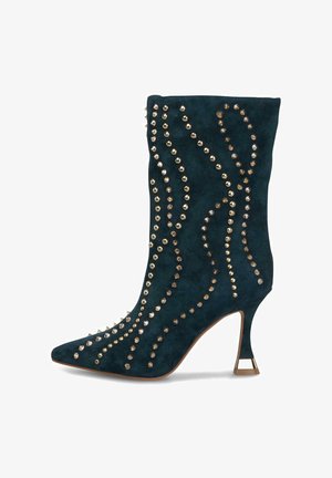 Bottine en suède noire à bout pointu, à talon évasé de hauteur intermédiaire, et ornée de clous dorés décoratifs dans des motifs sinueux.