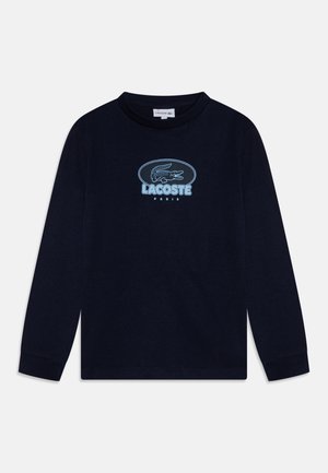 Granatowa koszula z długim rękawem z jasnoniebieskim logo krokodyla Lacoste i napisem "LACOSTE PARIS" na środku klatki piersiowej.