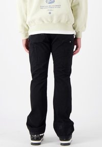 Zwarte cargobroek met een losse pasvorm, voorzien van zijzakken en een rafelige zoom. Draag een lichtgroene sweatshirt over een witte blouse.