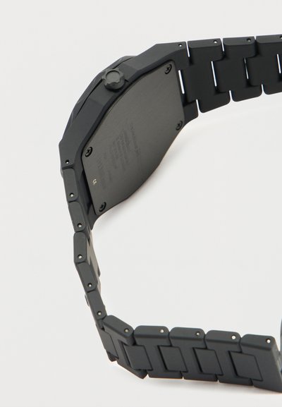 Μαύρο μεταλλικό ρολόι χειρός με ορθογώνια κάσα και σύνδεσμο βραχιολιού, που δείχνει την πίσω πλευρά στερεωμένη με τέσσερις βίδες και μια πλευρική κορόνα.