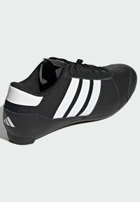 Svart sportig sko med texturerad ovandel, utrustad med tre vita ränder, ett perforerat område och en rundad tådesign.