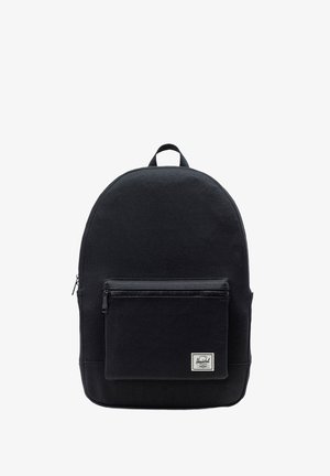 Sac à dos noir en tissu durable, avec une forme arrondie, une poche zippée à l'avant, et un petit accent de label en bas.