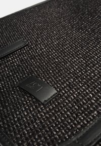 Zwarte geweven stof met een gestructureerd oppervlak en een donker leren accent met reliëfbranding. Rechthoekige vorm, minimalistisch ontwerp.