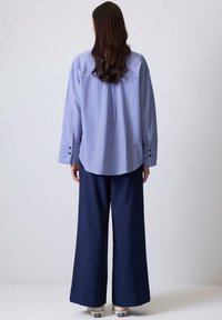 Camisa de rayas azules con mangas largas y puños con botones, combinada con pantalones de pierna ancha en color navy. Textura suave, corte relajado.