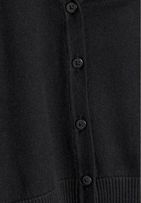 Gros plan sur un tissu de cardigan noir avec cinq boutons noirs fixés le long de la patte de boutonnage côtelée.