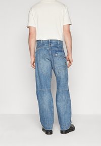 Hellblaues Denim-Jeans mit lockerer Passform, einem runden Taschendesign, Gürtelschlaufen und einem Detail an der Gesäßtasche.