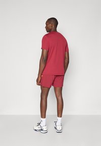 Red sports t-shirt and shorts made from lightweight fabric, paired with white athletic shoes and white socks. Simple design, comfortable fit.