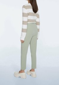 Pull court à rayures beiges et blanches, associé à un pantalon vert clair taille haute et cintré, ainsi qu'à des chaussures blanches à semelles épaisses.