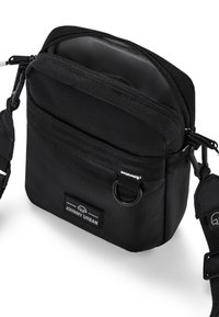 Borsa a tracolla nera in tessuto con chiusura a zip, tracolla regolabile, tasca frontale e logo impresso. Design compatto e rettangolare con superficie testurizzata.