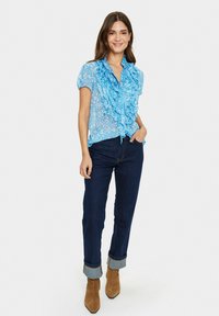 Ljusblå volangblus med korta ärmar, prydd med ett blommönster. Tillsammans med mörka denimjeans med uppvände ärmslut och bruna ankelboots.