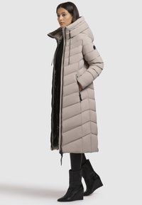 Pikk, patjadega puffjakke heles beežis, millel on kõrge krae, lukku sulgemine ja küljetaskud. Kombineeritud mustade platvormine jalatsitega.