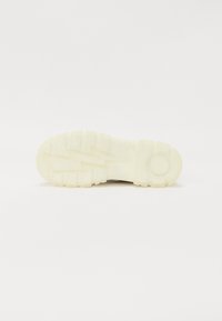 Chunky gumowa podeszwa sneakerów w kolorze off-white, z głębokimi rowkami i wzorem zygzaka dla lepszej przyczepności; okrągły akcent przy pięcie.