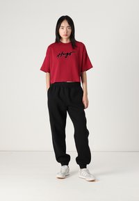 Rode t-shirt met korte mouwen met zwart geborduurd "Hugo" logo, gecombineerd met zwarte joggers met elastische tailleband en grijze sneakers. Effen kleuren, ontspannen pasvorm.